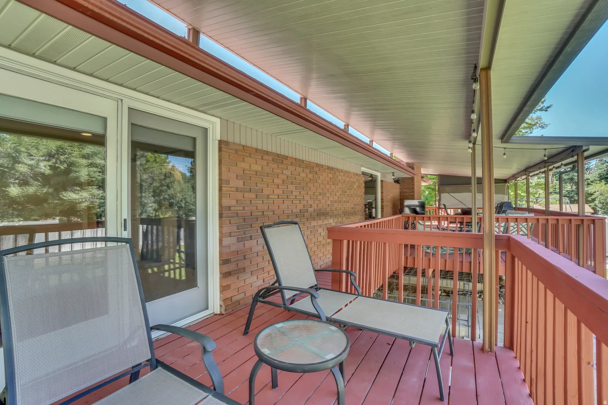 Expansive red-stained wood covered deck featuring a covered area, white vinyl soffit, and brick exterior