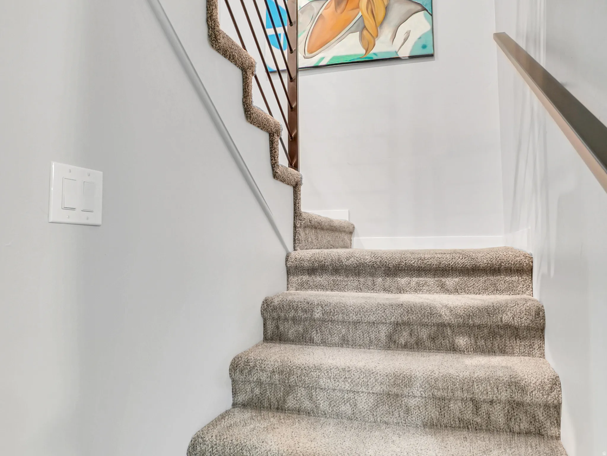Carpeted staircase with modern vertical metal balusters and a wood handrail
