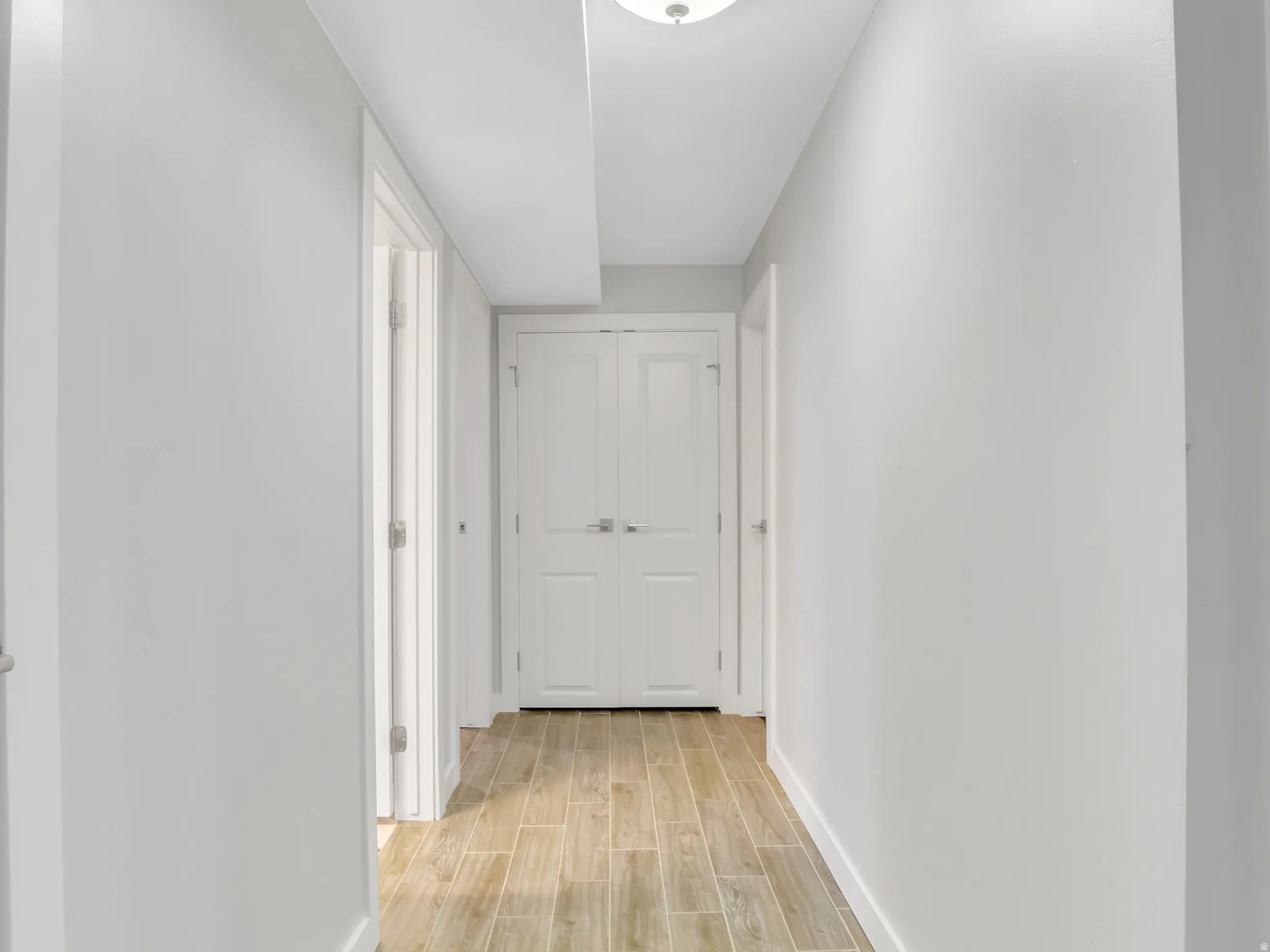 Hallway featuring wood-finish flooring, white baseboards, and a flush-mount ceiling light fixture