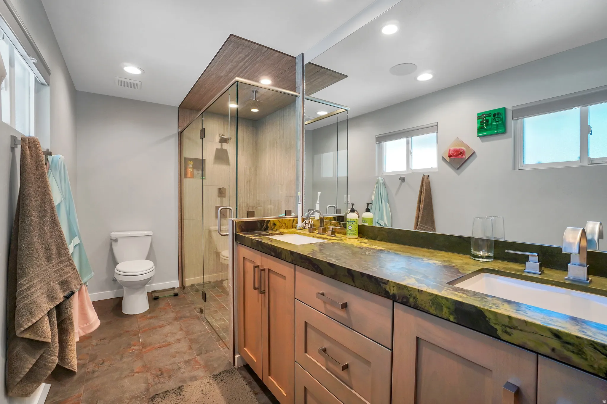 Bathroom featuring a dual vanity with a green stone countertop, light wood cabinetry, and integrated sinks
