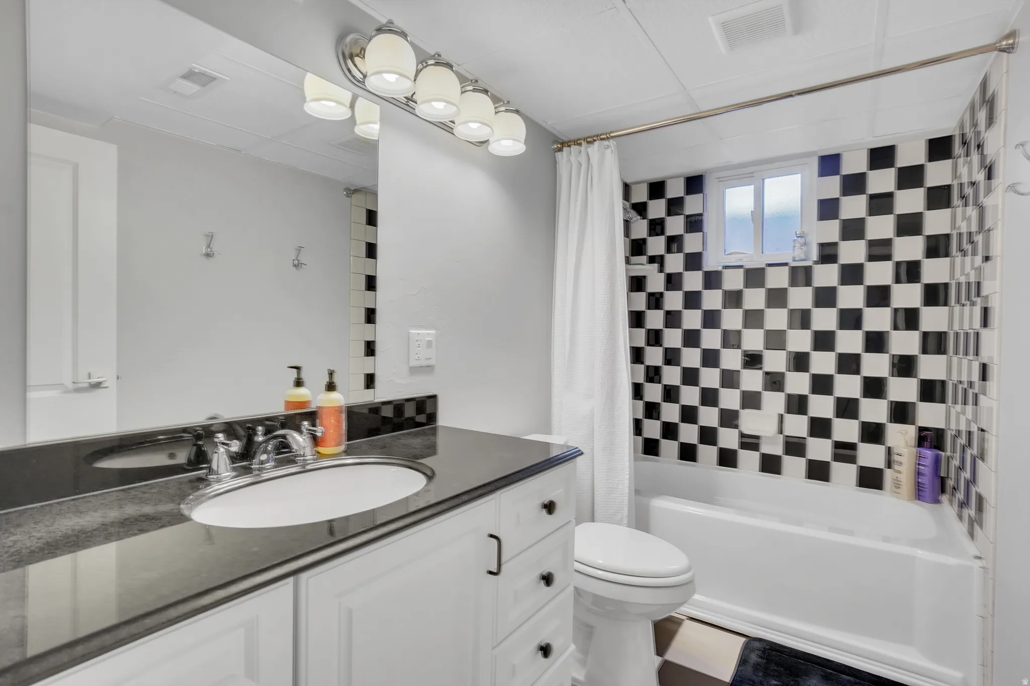 Bathroom featuring a black and white checkered tile tub surround, white bathtub, and vanity with an integrated sink and dark countertop
