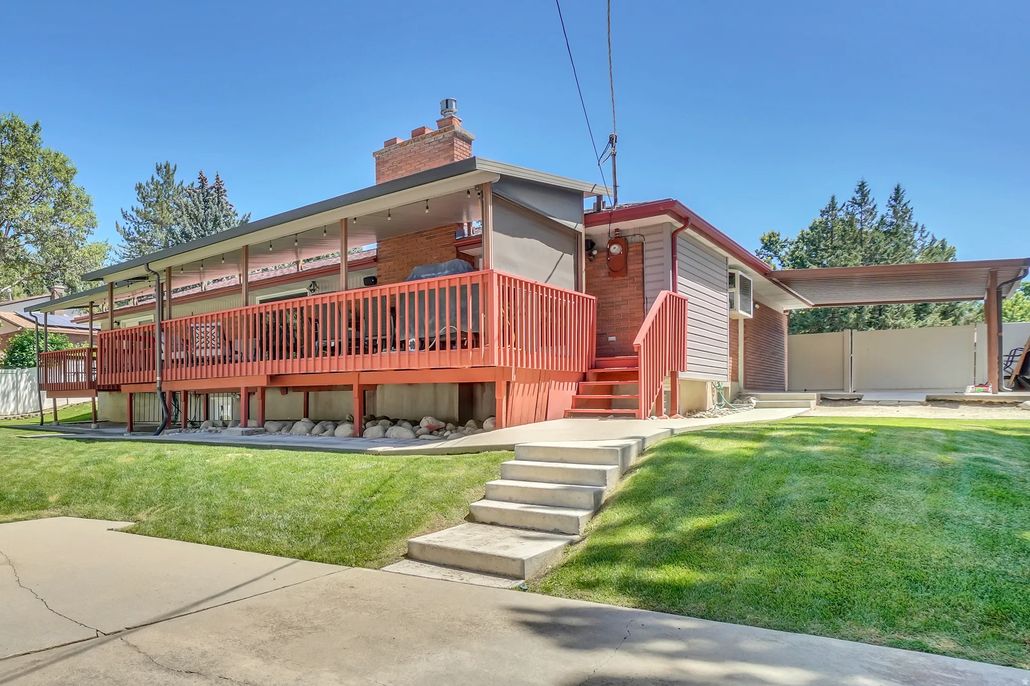 Exterior featuring a large elevated deck with wood railing, covered patio space, brick chimney, and an attached carport