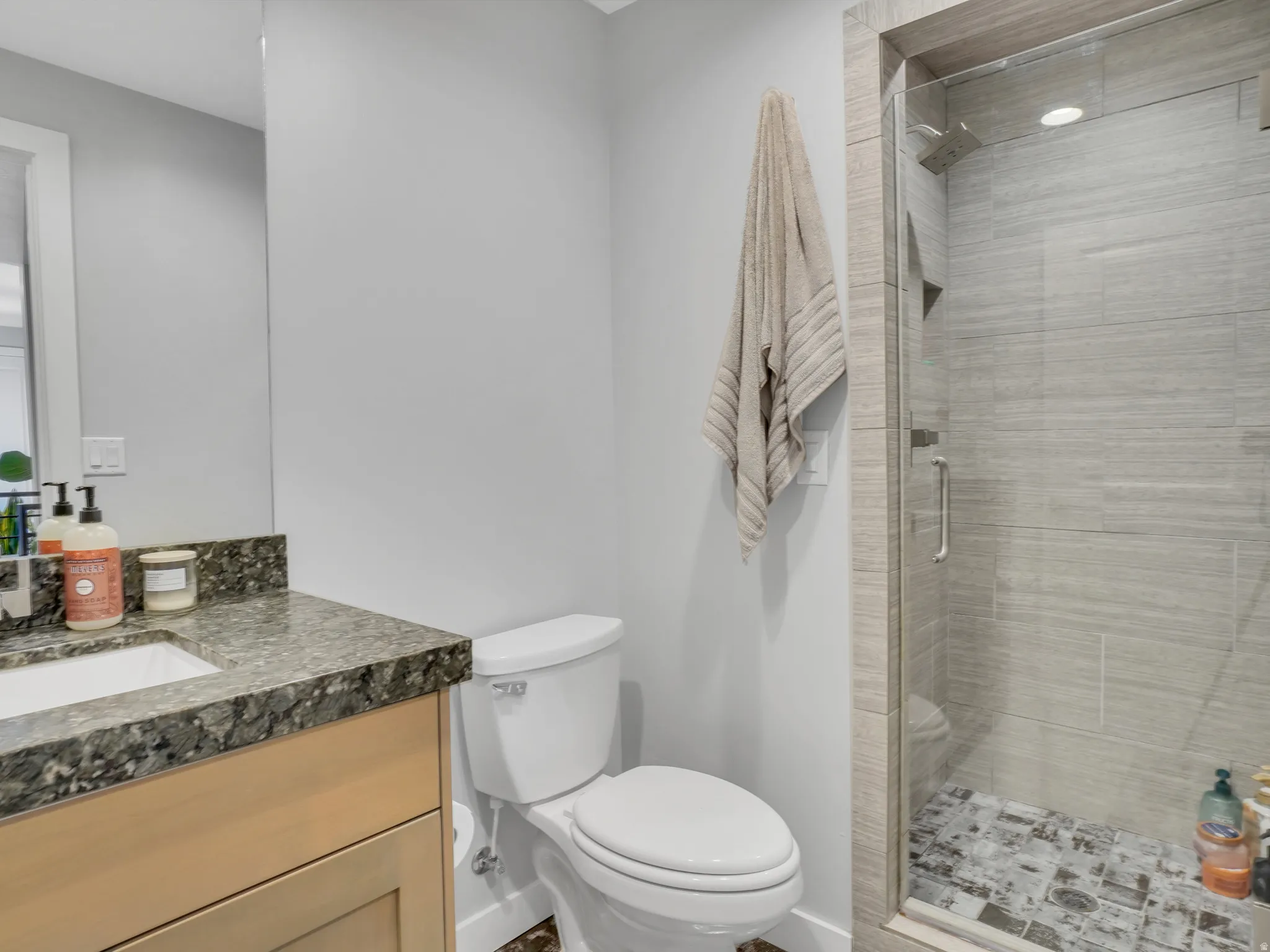 Contemporary bathroom featuring a glass-enclosed shower with horizontal tile walls and a mosaic tile floor, alongside a vanity with a dark granite countertop and an undermount sink