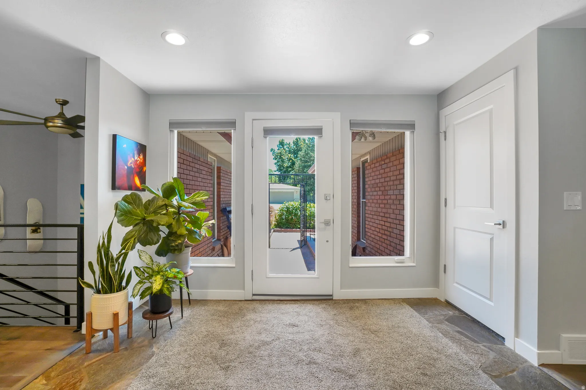 Entryway featuring a full-light glass door flanked by two side windows, recessed ceiling lighting, a modern paneled interior door, and a multi-level flooring treatment with carpet and stone-finish tiles