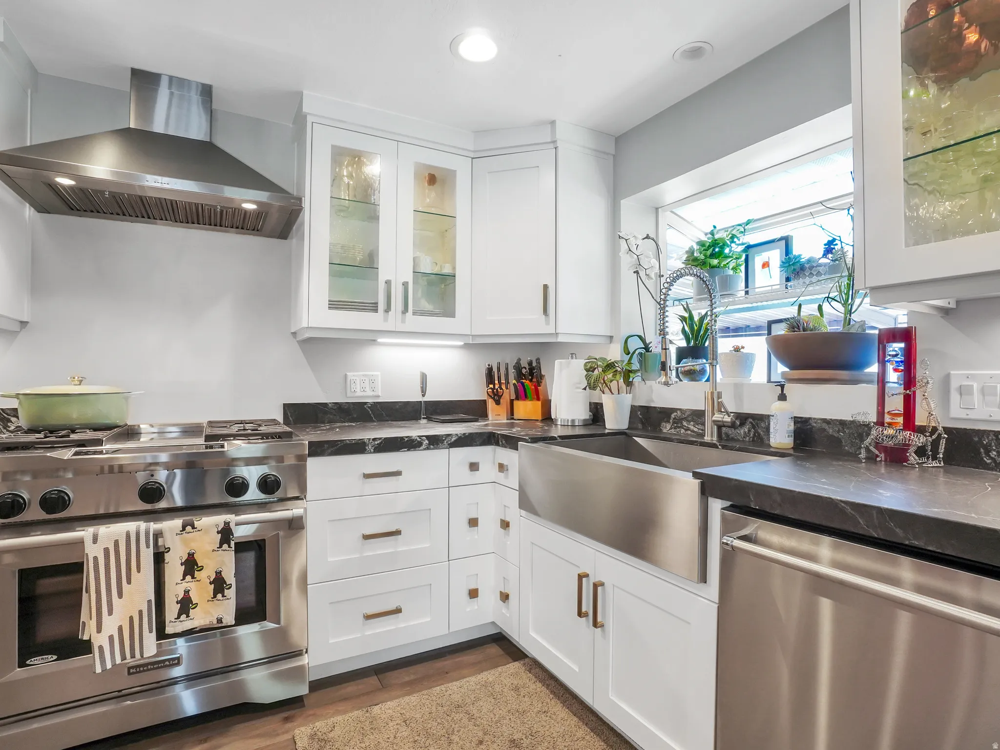 Contemporary kitchen featuring white cabinetry with bronze hardware, dark stone countertops, and a stainless steel farmhouse sink