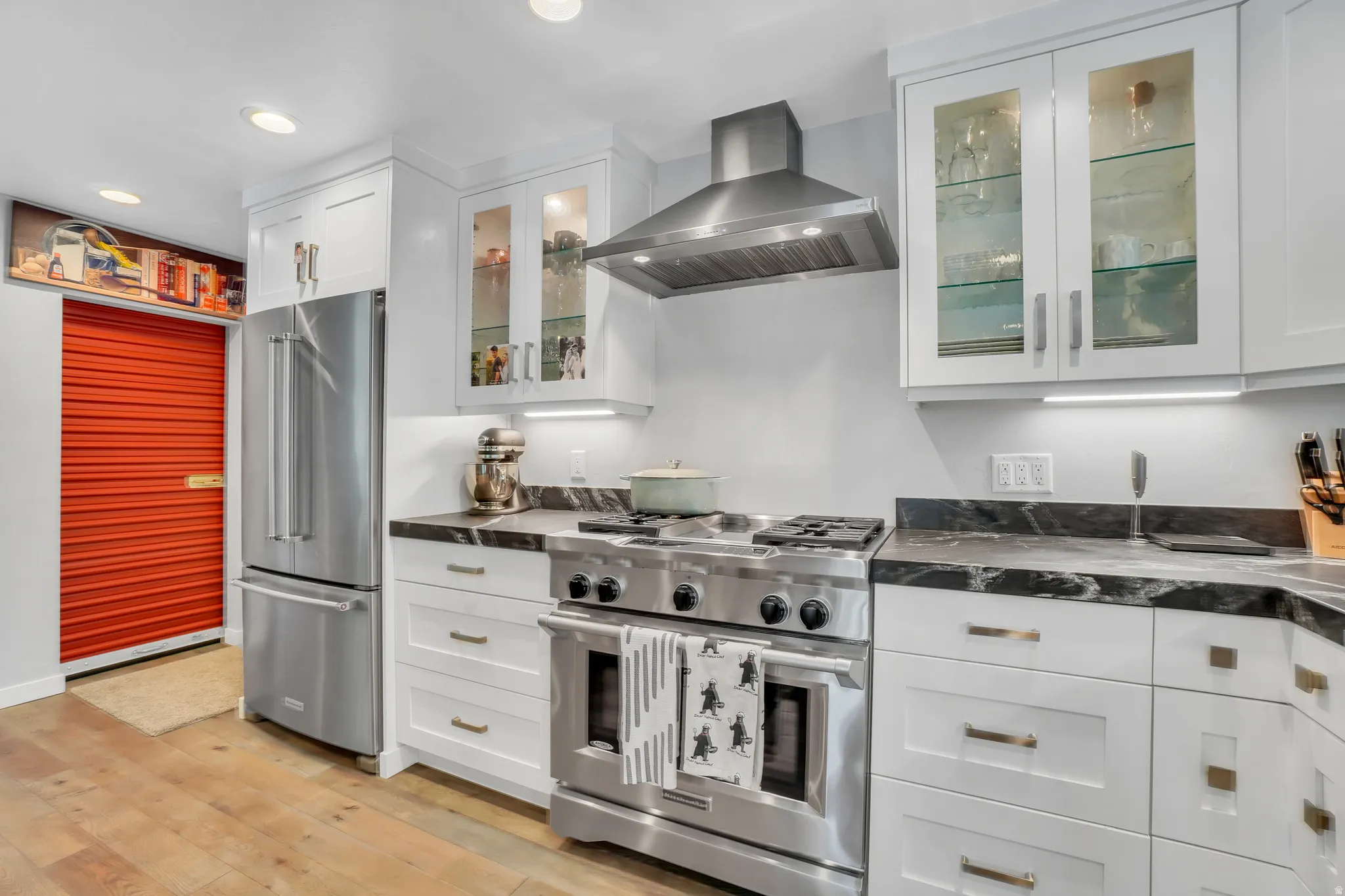 Gourmet kitchen featuring stainless steel appliances, dark stone countertops, white shaker cabinetry with glass-front uppers, and wood-finish flooring