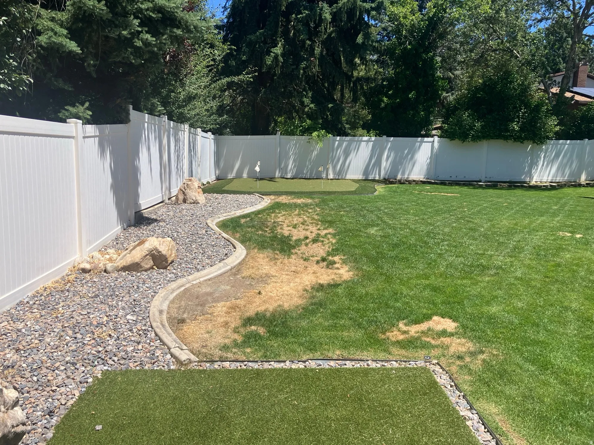 Expansive backyard featuring a putting green, a white privacy fence, and a gravel bed with decorative boulders