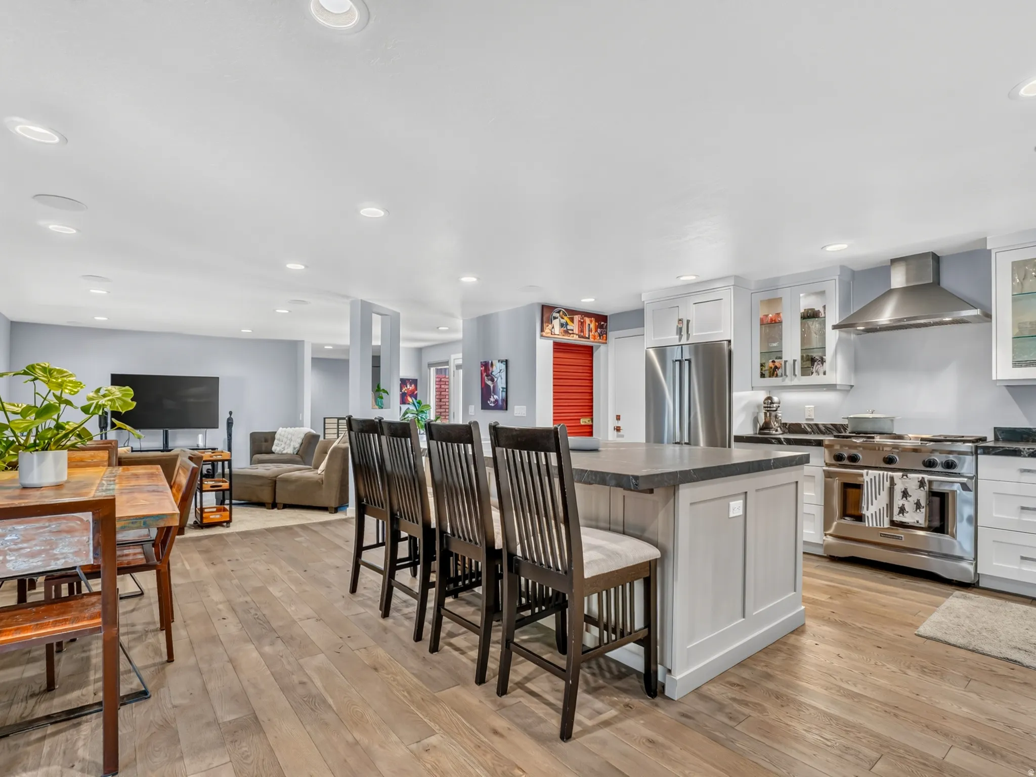 Open-concept kitchen featuring an oversized island with seating, stainless steel appliances, white cabinetry, dark countertops, and wood-finish flooring throughout