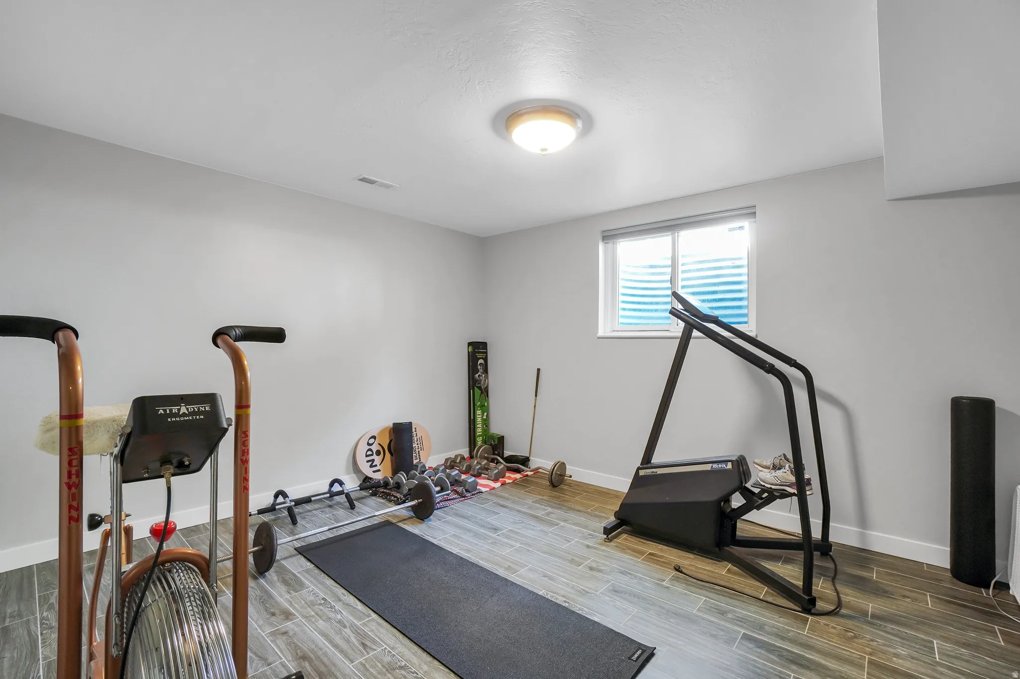 Versatile room featuring light gray walls, wood-finish flooring, and a flush-mount ceiling light