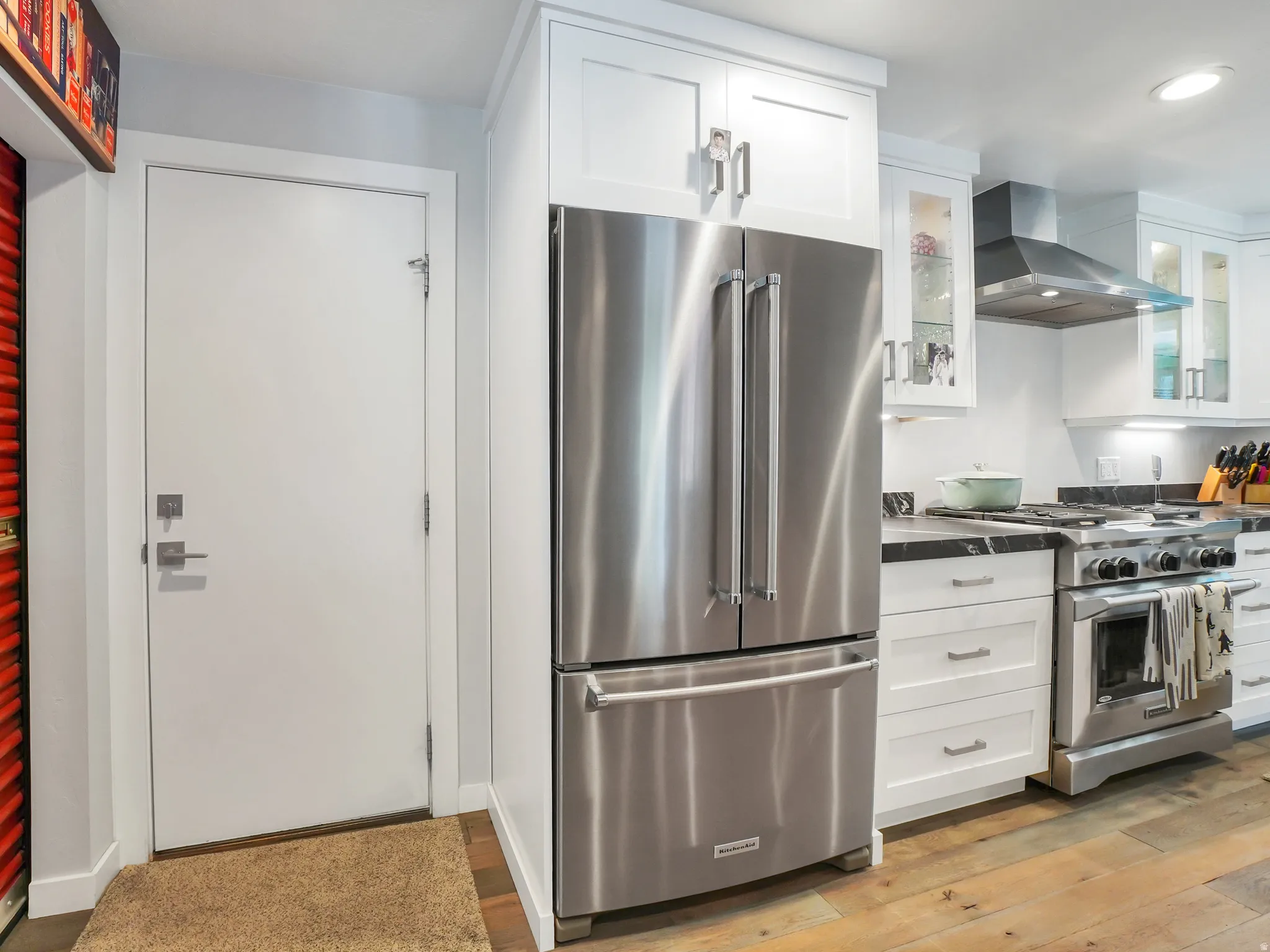 Modern kitchen featuring stainless steel appliances, white shaker cabinetry, dark countertops, a professional-grade range with a stainless steel hood, and wood-finish flooring