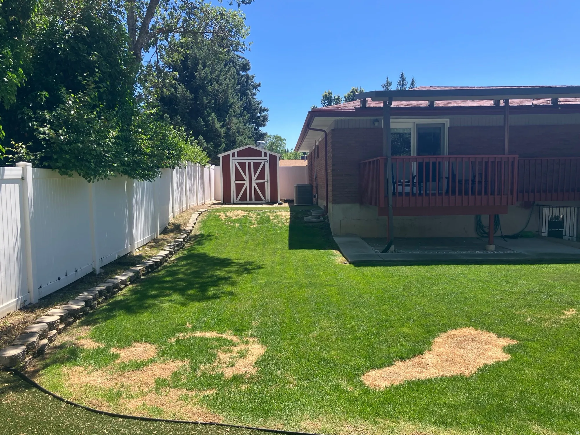 Expansive backyard featuring chipping area, a manicured lawn, white privacy fencing, and a versatile storage shed