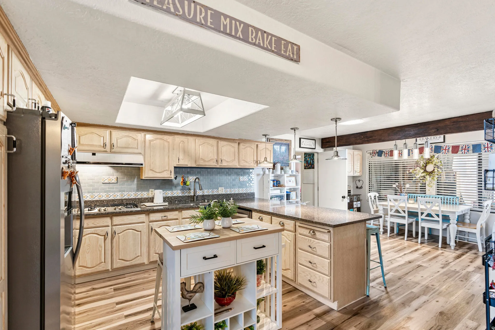 Kitchen featuring wood-finish flooring, light wood cabinetry, a central island with a solid surface countertop, and a skylight
