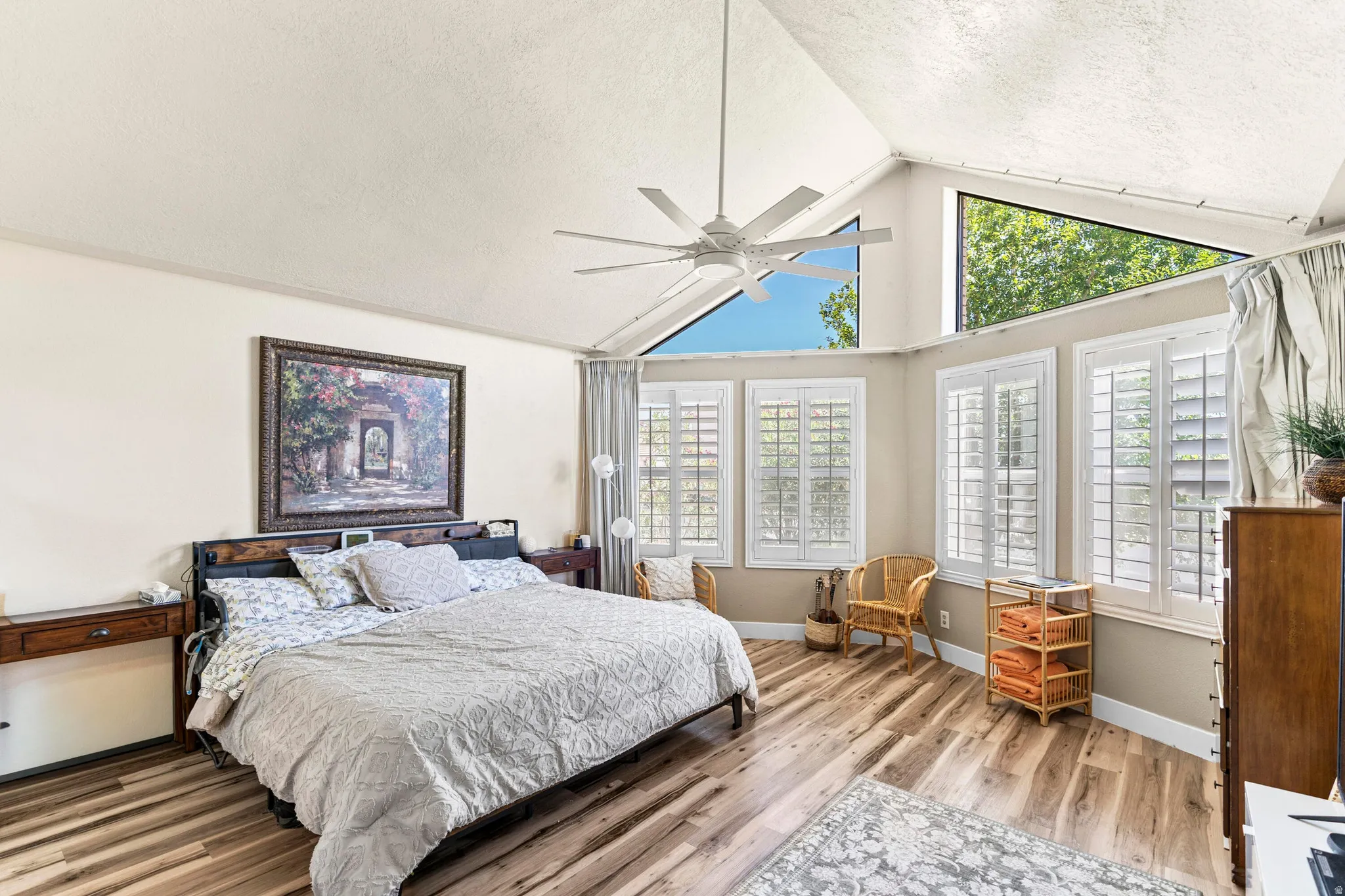 Vaulted ceiling bedroom featuring wood-finish flooring, multiple windows with white plantation shutters, and high-set triangular windows