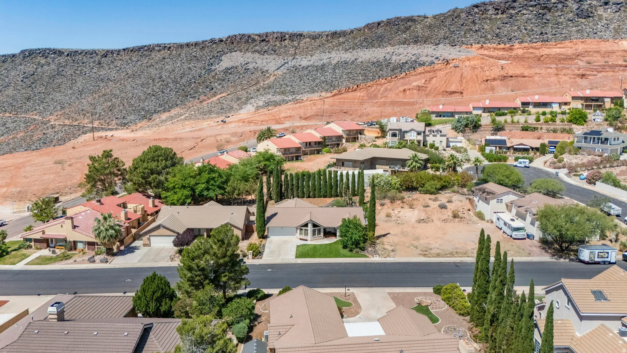 Terraced homes nestled against a rugged mountain landscape with mature trees and paved roadways