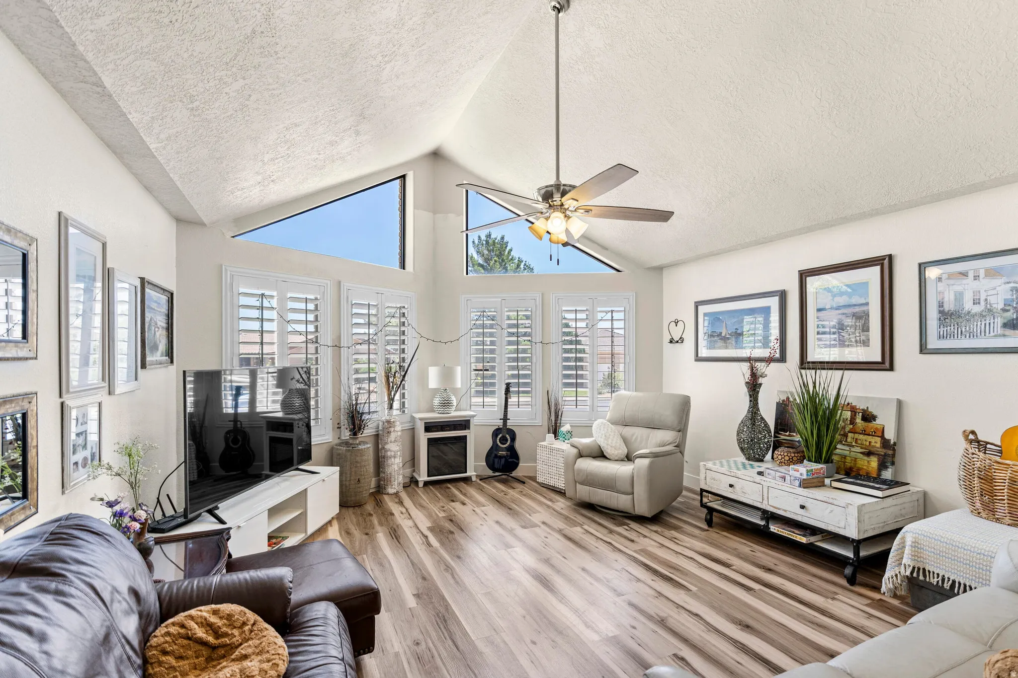 Living area featuring vaulted ceilings, clerestory windows, wood-finish flooring, a ceiling fan, and white window shutters