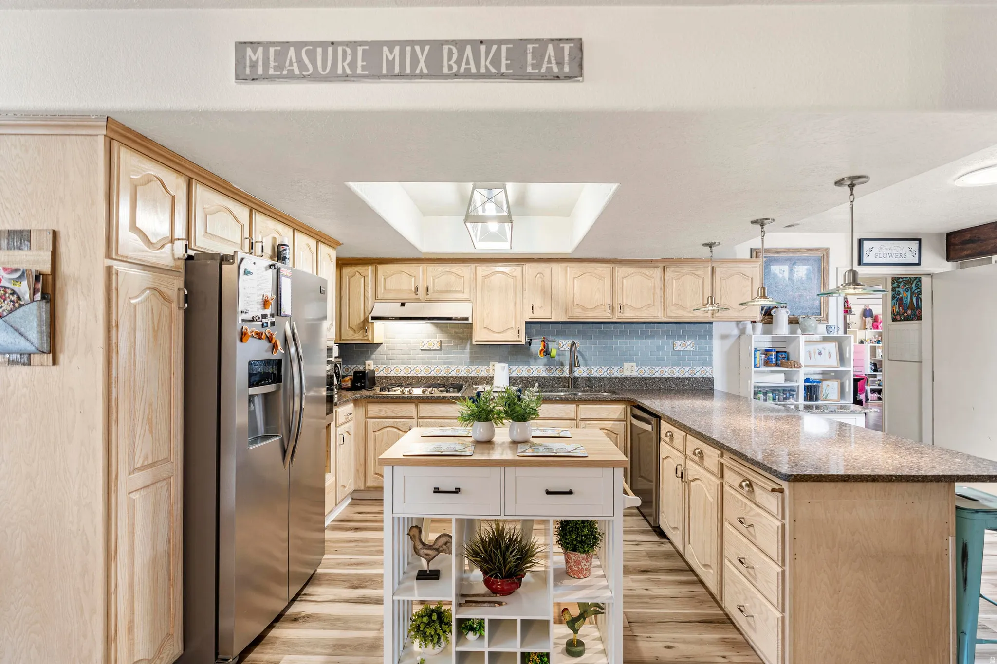 Kitchen featuring a central island, light wood-finish cabinetry, stainless steel appliances, and a skylight