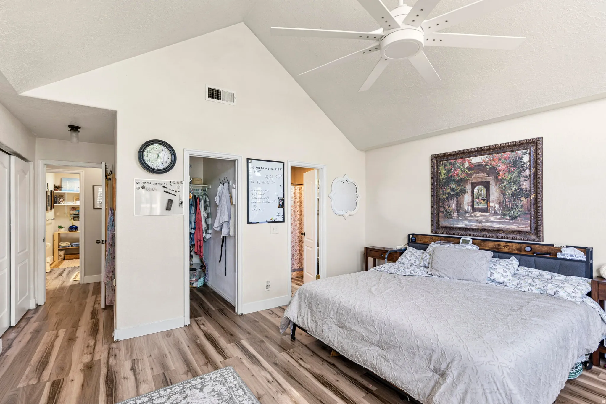 Vaulted ceiling with a white ceiling fan, wood-finish flooring, and white baseboards