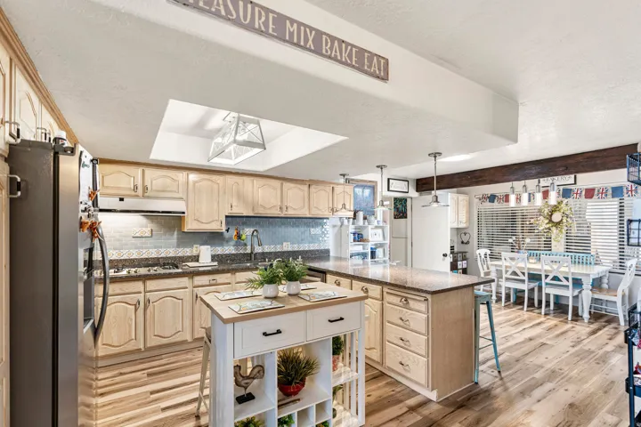 Kitchen featuring wood-finish flooring, light wood cabinetry, a central island with a solid surface countertop, and a skylight