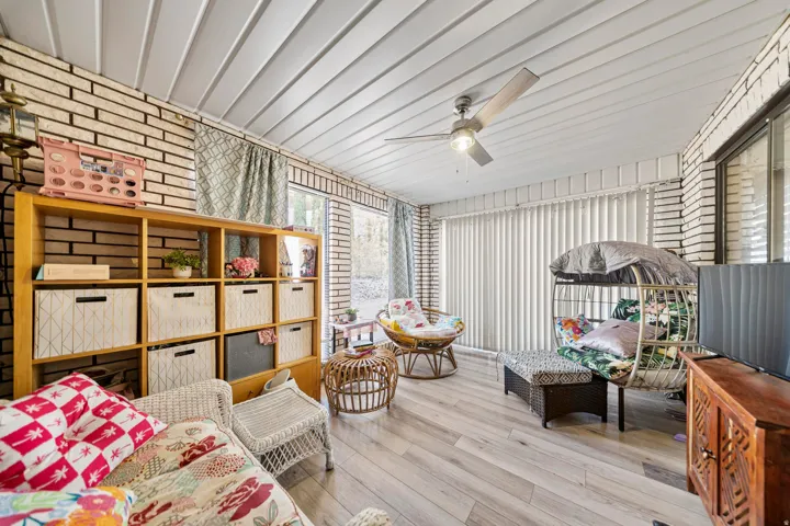Enclosed room featuring light-colored brick walls, wood-finish flooring, a white paneled ceiling, and a ceiling fan with integrated lighting