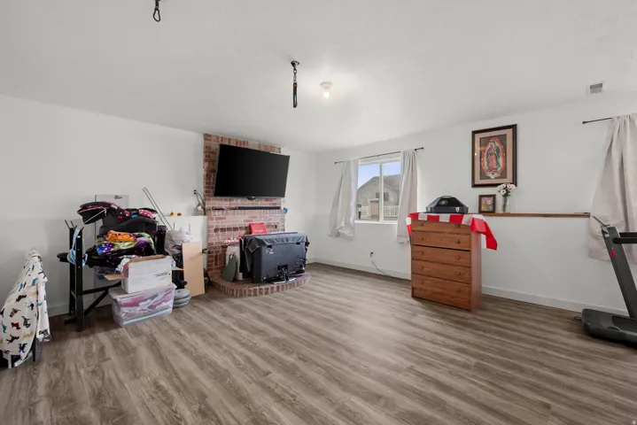 Spacious interior room featuring wood-finish flooring, white walls, and a prominent red brick fireplace