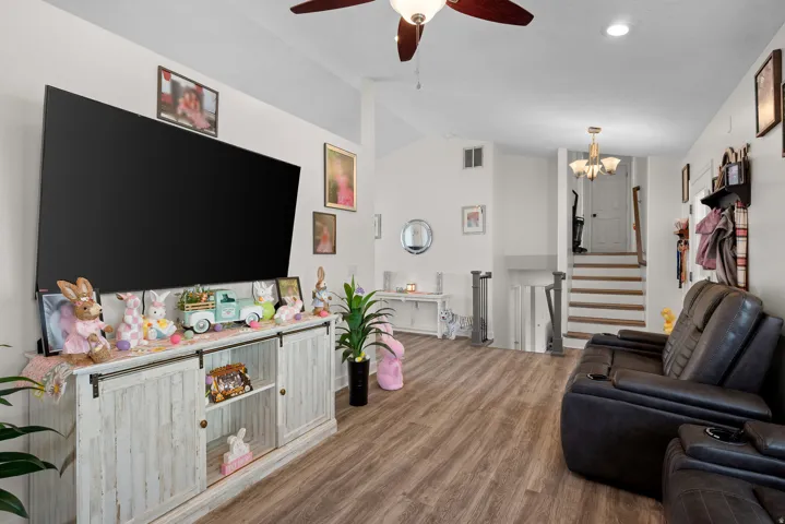 Spacious living area featuring wood-finish flooring, vaulted ceilings, and a ceiling fan with integrated lighting