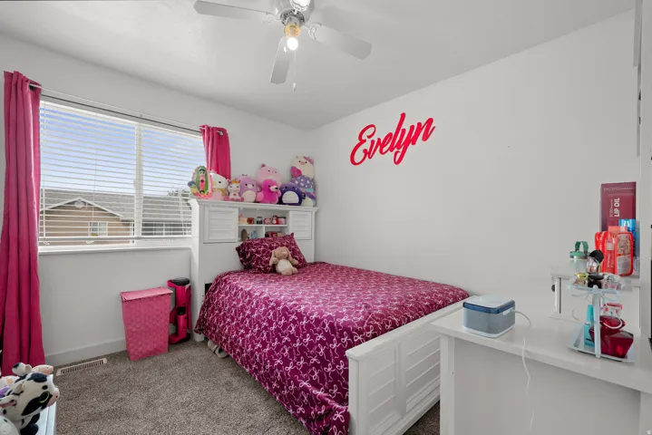 Carpeted bedroom featuring a ceiling fan, a window with horizontal blinds, and a built-in white shelving unit