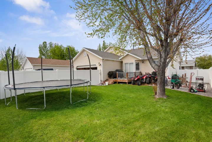 Expansive backyard with a manicured lawn, full privacy fencing, and a mature deciduous tree