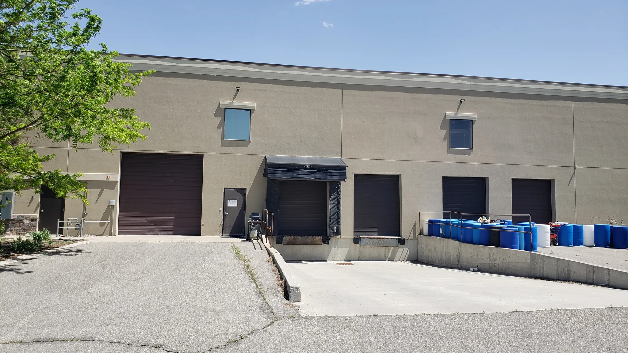 Industrial building featuring a stucco exterior, multiple loading dock doors, a large drive-in door, and an exterior personnel door