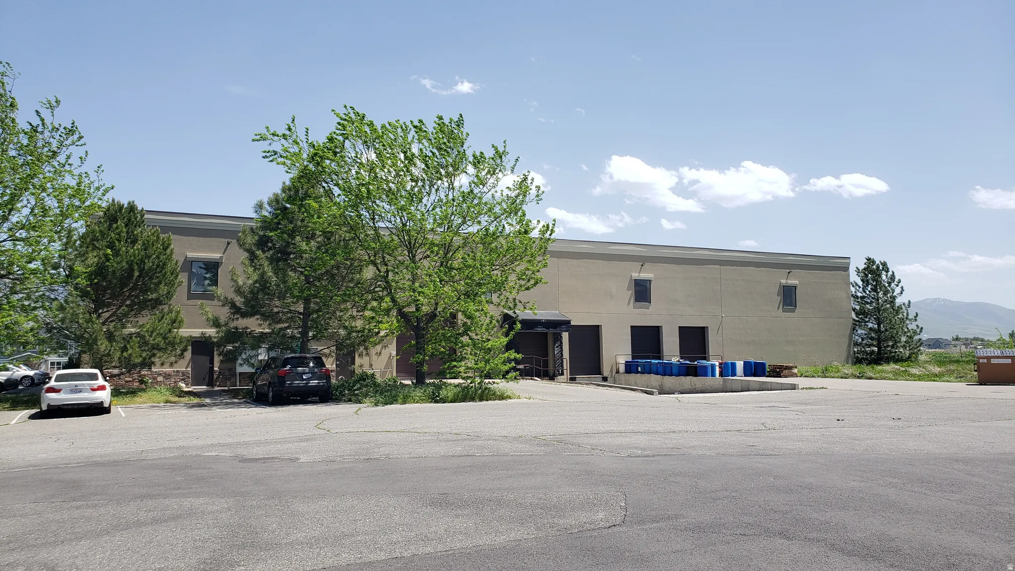 Commercial building featuring a large paved parking area, multiple roll-up doors for access, and a loading dock