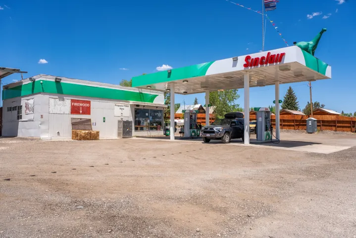 Commercial property featuring a gas station canopy with multiple fuel pumps, a retail building with a window display, and a gravel lot