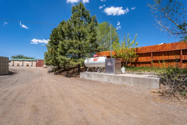 Propane tank on concrete pad with utility box, surrounded by mature trees and a wood fence