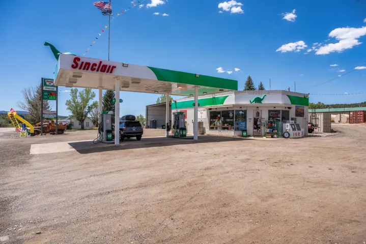 Sinclair gas station featuring multiple fuel pumps, a retail building with display windows, a wide unpaved lot, and a prominent gas price sign