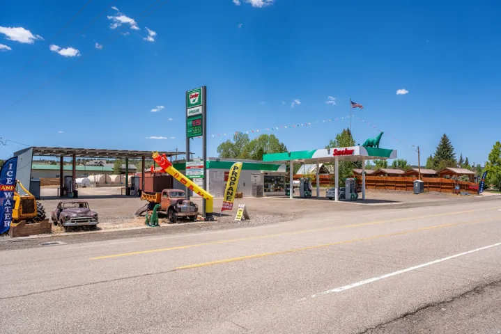 Commercial property featuring a gas station canopy with multiple fuel pumps, a separate covered parking or storage structure, and a paved road frontage