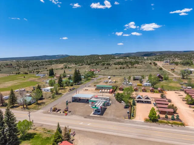 Expansive rural property featuring a gas station with covered pumps, multiple cabin-style structures, and additional buildings, all bordered by a paved road