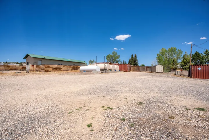 Expansive gravel lot featuring a long commercial building with a green roof, a large white storage tank, and various storage containers