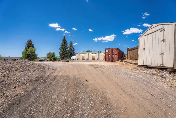 Gravel driveway with a light-colored utility shed, a red shipping container, and multiple storage tanks
