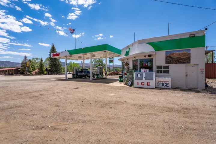 Commercial property featuring a gas station canopy with multiple pumps, an adjacent convenience store building, and a large unpaved lot