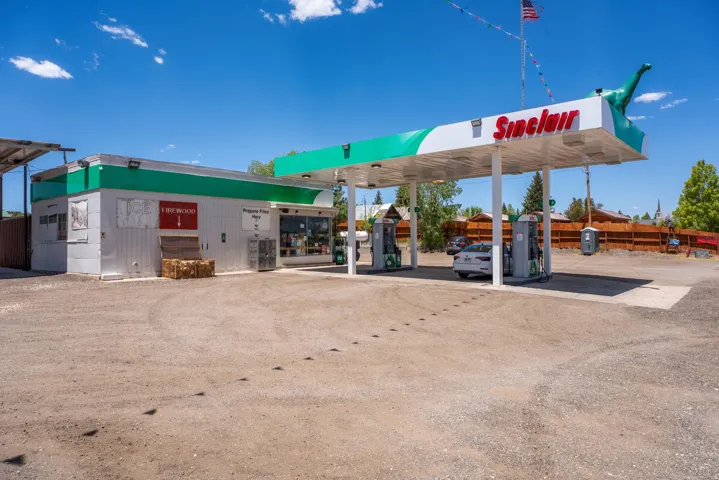 Commercial property featuring a Sinclair branded gas station canopy with multiple fuel pumps, an attached retail building, and a large gravel parking area
