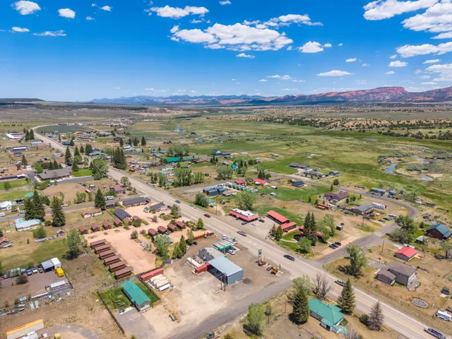 Expansive aerial capture of a community with a prominent roadway, surrounded by open grassland and distant mountains