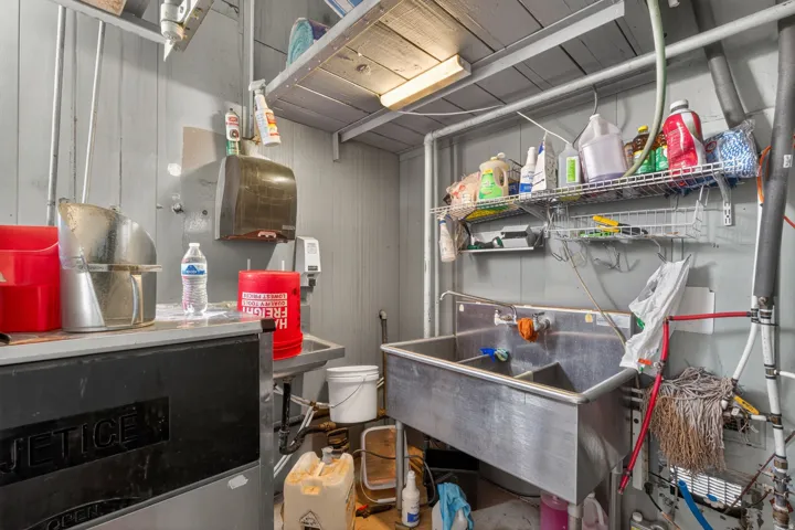 Utility room featuring a large stainless steel double basin sink, wall-mounted wire shelving, and wood-paneled walls