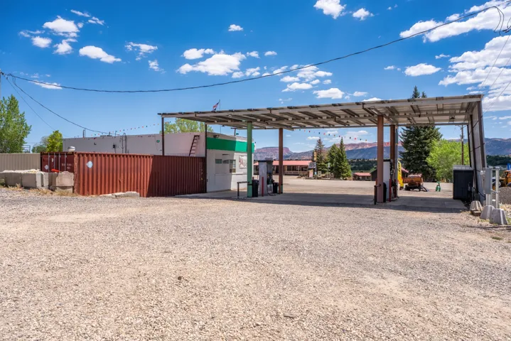 Commercial property featuring a fuel station canopy with multiple dispensers, an associated building with a green and white facade, and a large gravel lot