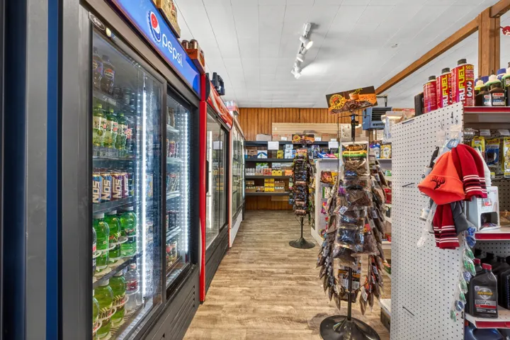 Commercial interior featuring multiple glass-front display refrigerators with integrated lighting, wood-finish flooring, a white acoustic tile ceiling with track lighting, and wood paneling accents