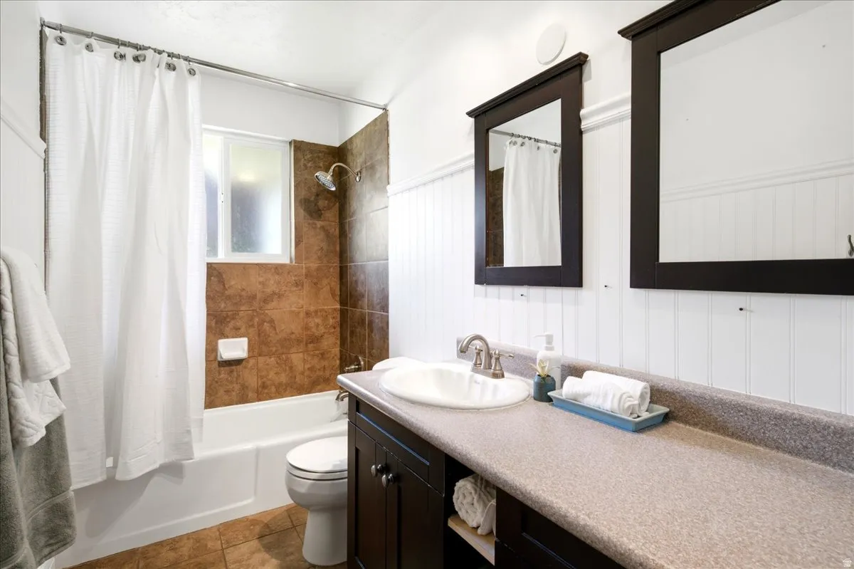 Bathroom featuring a dark wood double vanity with an integrated sink and a speckled countertop, framed mirrors, and white beadboard paneling
