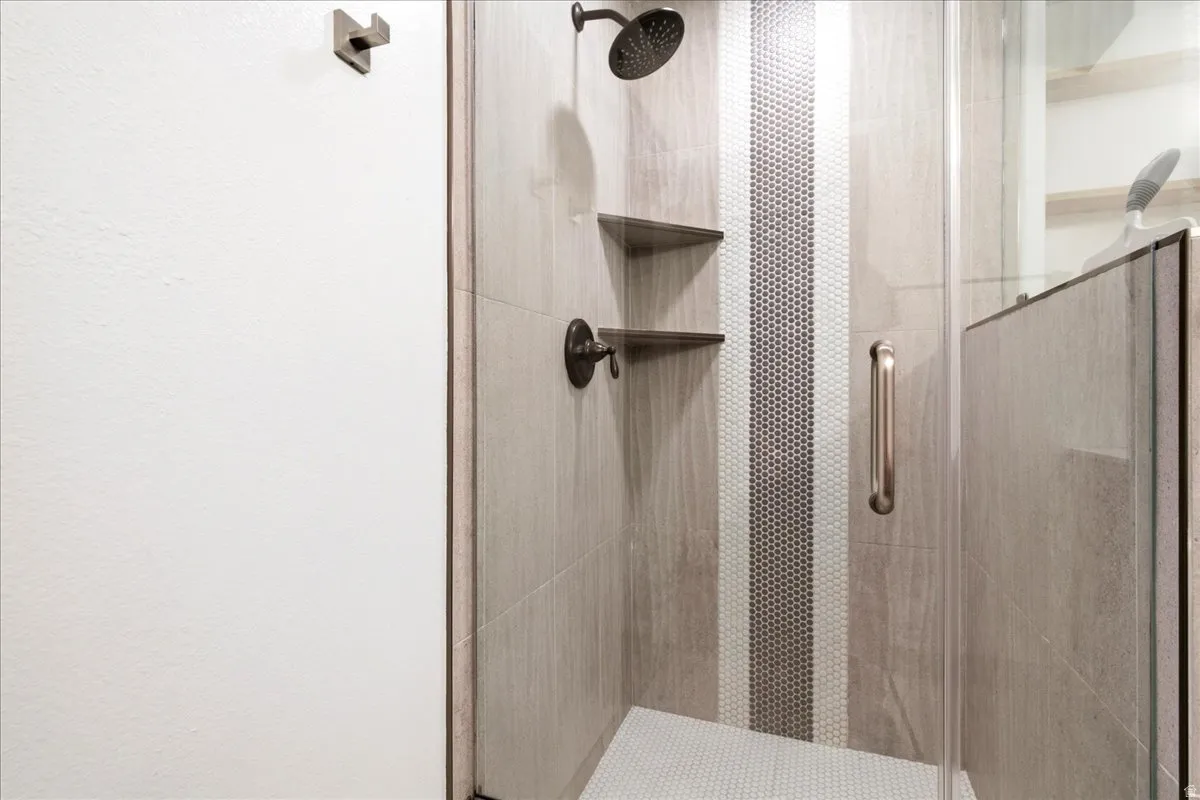Glass-enclosed shower featuring wood-finish wall tiles, a mosaic tile accent stripe, and a contrasting penny tile floor