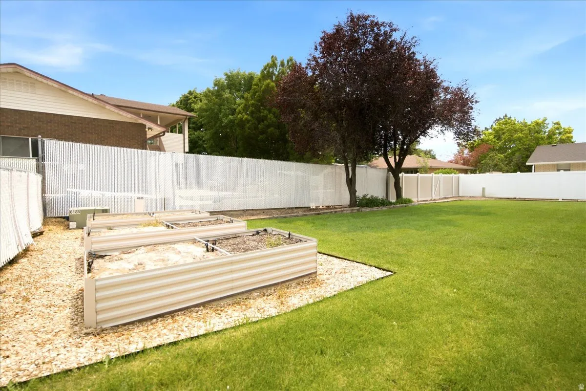 Expansive rear yard featuring a manicured lawn, established trees, privacy fencing, and raised garden beds with a gravel surround