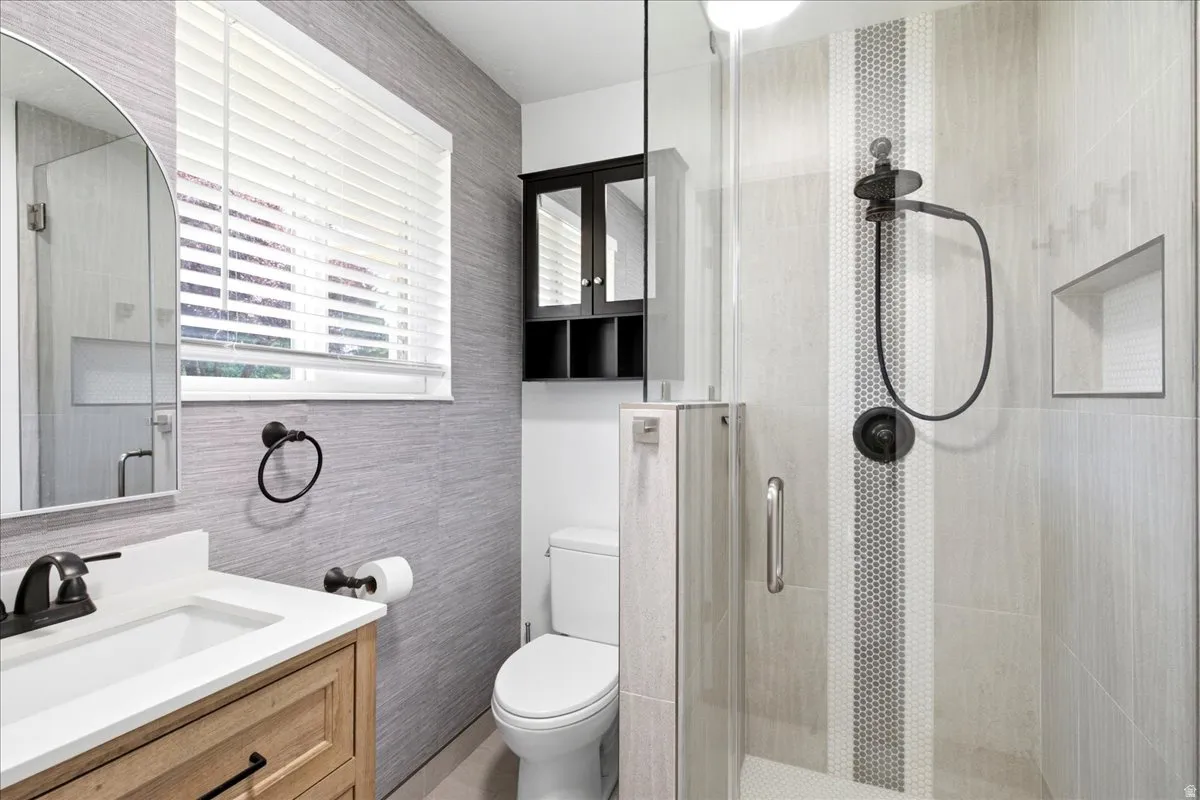 Master Bathroom featuring a glass-enclosed shower with a niche, a wood-finish vanity with a white countertop, and an arched mirror