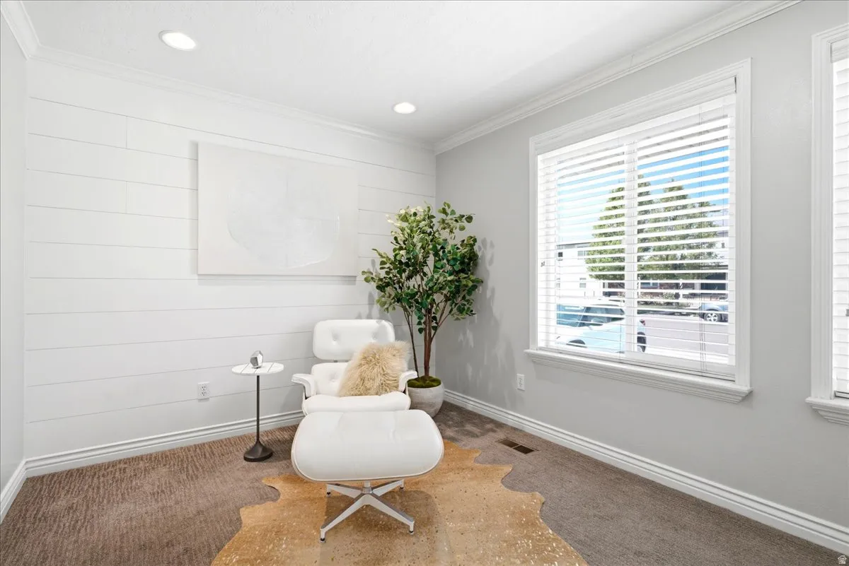Bright interior room featuring a prominent window with horizontal blinds, shiplap accent wall, recessed lighting, crown molding, and carpeted flooring