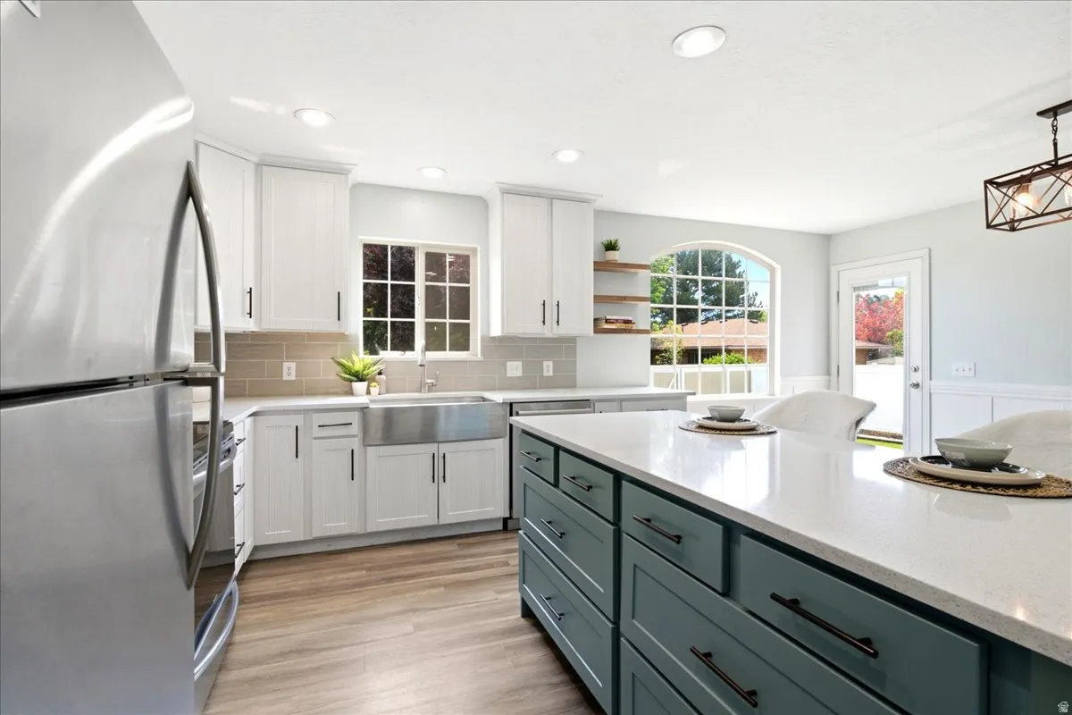 Open-concept kitchen featuring a large central island with a solid surface countertop, white shaker cabinetry, stainless steel appliances, and wood-finish flooring