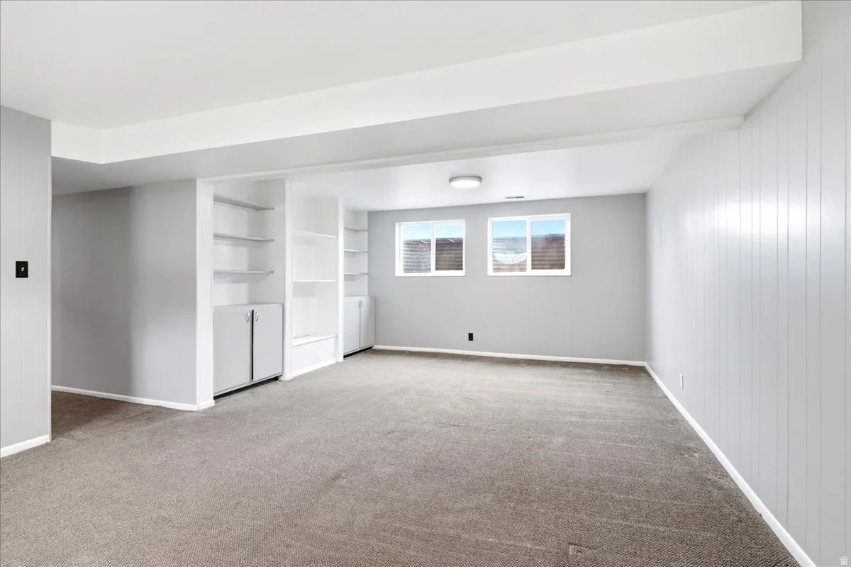 Carpeted room featuring two built-in shelving units with lower cabinetry, two windows, and vertical paneling on one wall