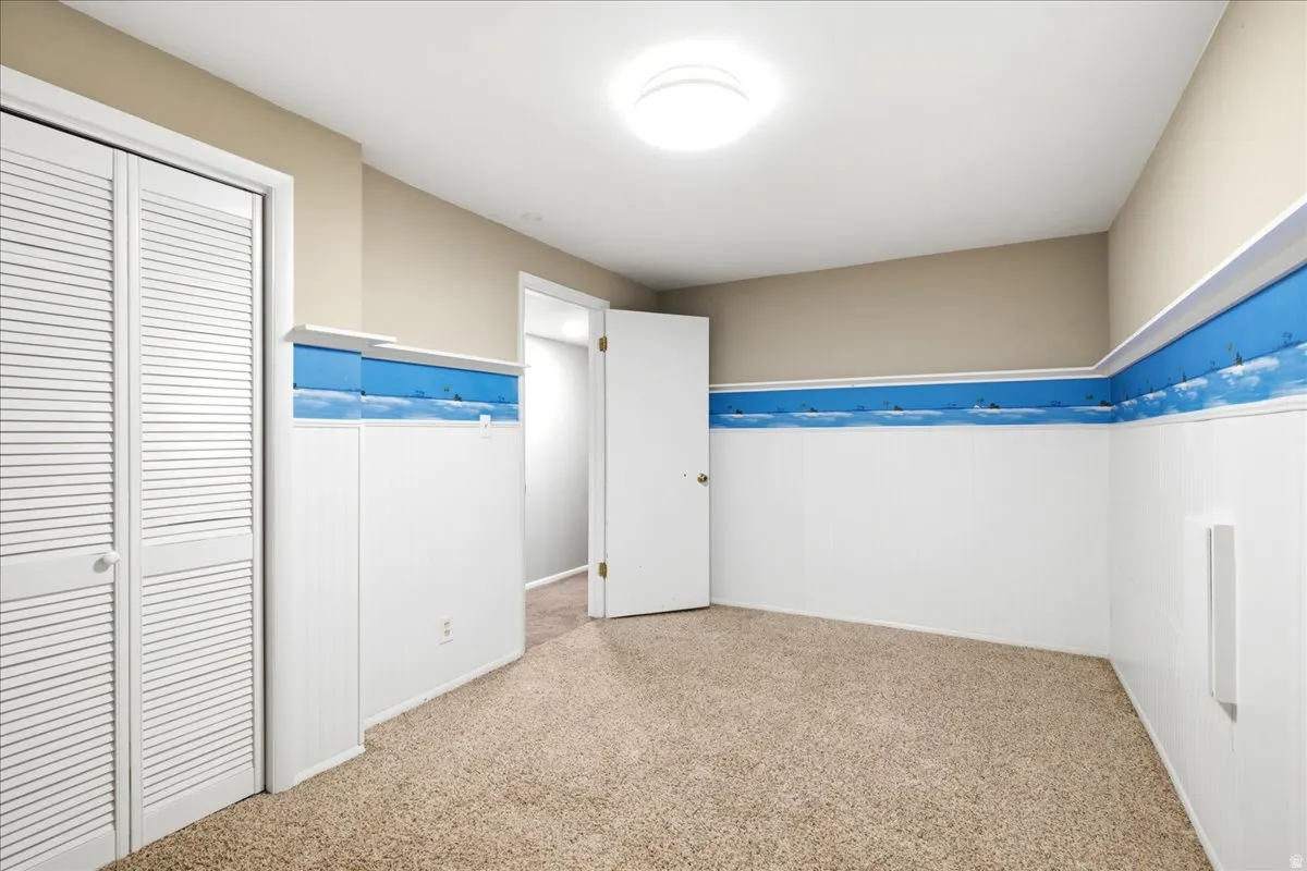 Carpeted room featuring white bi-fold louvered closet doors, wainscoting with a blue decorative border, and a ceiling-mounted light fixture